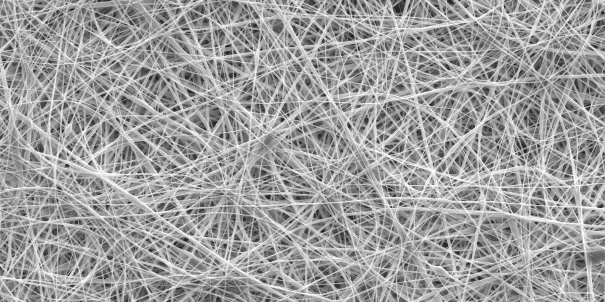 Close-up image of a dense network of thin, white fibers crisscrossing in random directions, creating a complex web-like texture against a dark background.