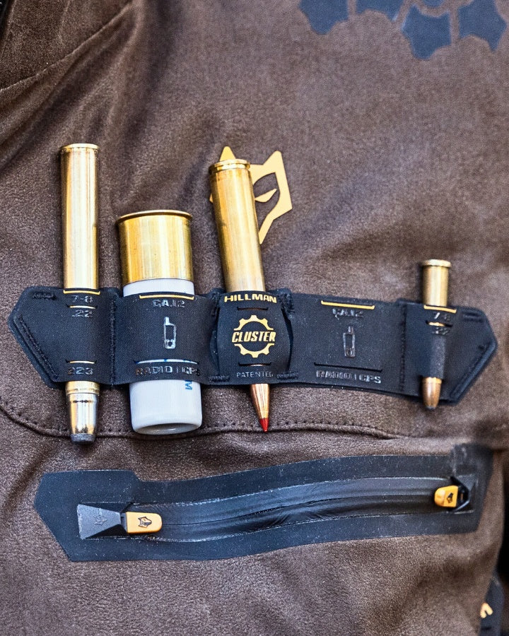 Close-up of a brown jacket with a pocket organizer holding four gold and silver bullet-shaped pens. Each pen is individually secured, and theres also a zippered pocket with a gold zipper pull below the organizer.