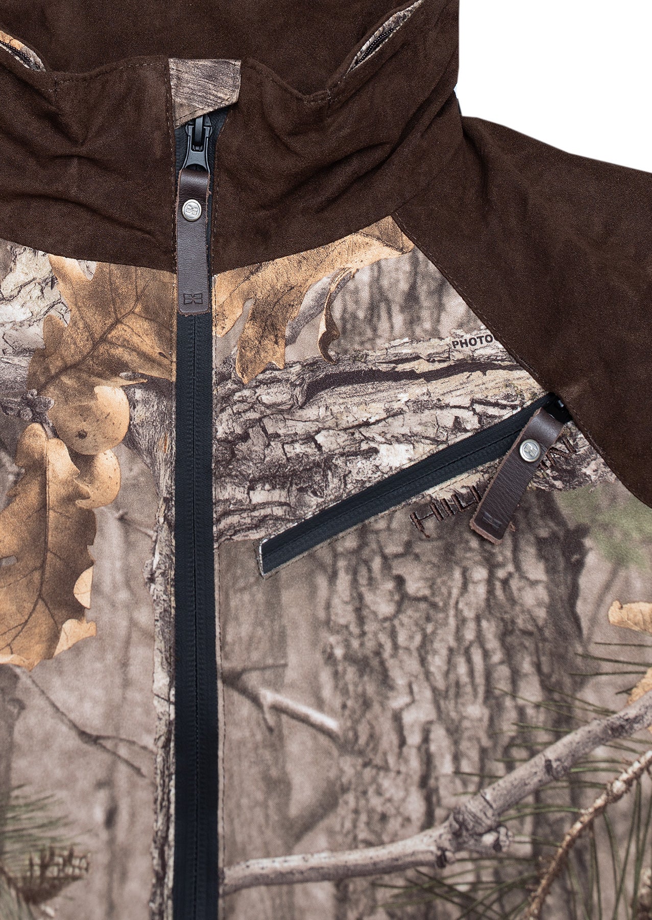 Close-up of the Hillman Fusion Hunting Jacket 3DX, showing its tree bark and leaf camouflage, dark brown hood and shoulders, black front zipper, and chest pocket with a leather pull tab.